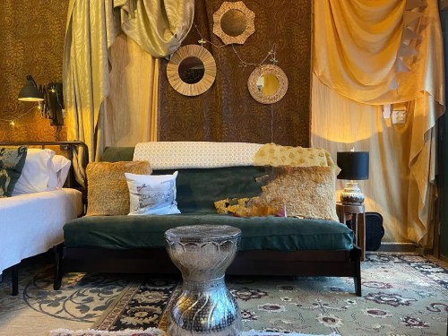 Cozy living space with a green sofa, decorative pillows, mirrors, and warm lighting against a textured wall.
