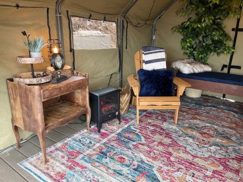 Cozy interior of a tent featuring a wooden desk, chair, decorative rug, and a small electric heater.