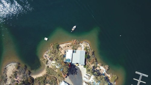 Aerial view of a serene waterway with a small boat near a landscaped shore and a building surrounded by greenery.