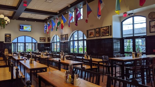 Interior of a spacious restaurant with wooden tables, chairs, and various flags hanging from the ceiling.
