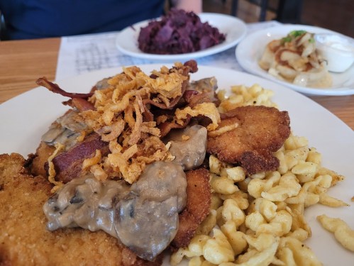 A plate of fried chicken topped with gravy and crispy onions, served with macaroni and cheese and a side of red cabbage.
