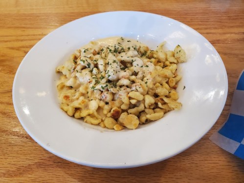 A white bowl filled with small pasta pieces topped with creamy sauce and herbs, placed on a wooden table.