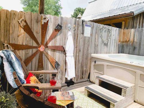 A cozy outdoor spa area with a hot tub, wooden fence, and a robe hanging on the wall, surrounded by decorative items.