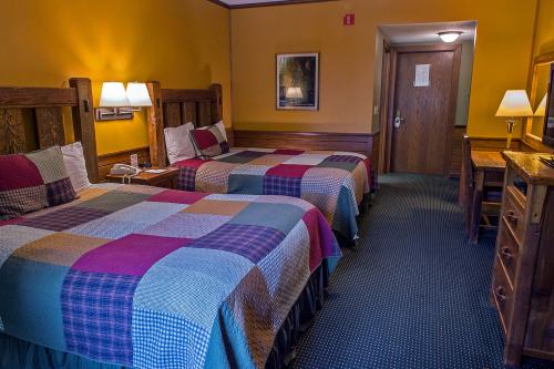 A cozy hotel room with two beds, colorful quilts, wooden furniture, and warm yellow walls.