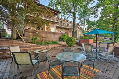 A cozy outdoor patio with seating, a table, and an umbrella, surrounded by greenery and a wooden deck.