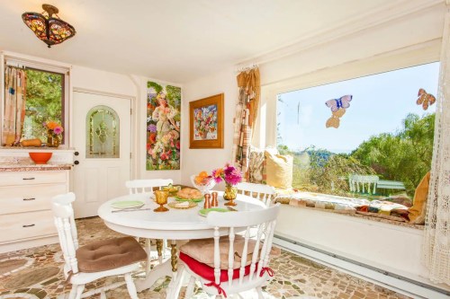 Bright, cozy dining area with a round table, floral decor, and a large window showcasing a scenic view.