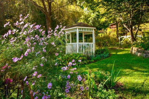 A charming white gazebo surrounded by vibrant flowers and lush greenery in a serene garden setting.