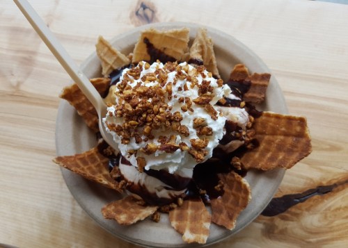 A bowl of ice cream topped with whipped cream, chocolate sauce, and crunchy waffle pieces.