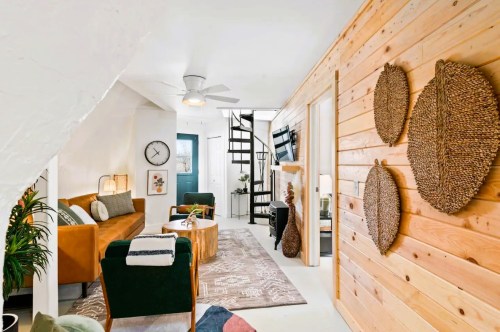 Cozy living space with a brown sofa, green chairs, wooden accents, and a spiral staircase leading to an upper level.