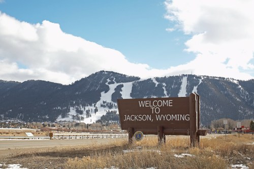 A welcome sign for Jackson, Wyoming, with snow-capped mountains and a blue sky in the background.
