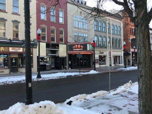 A snowy street scene featuring a theater marquee and festive decorations on buildings.