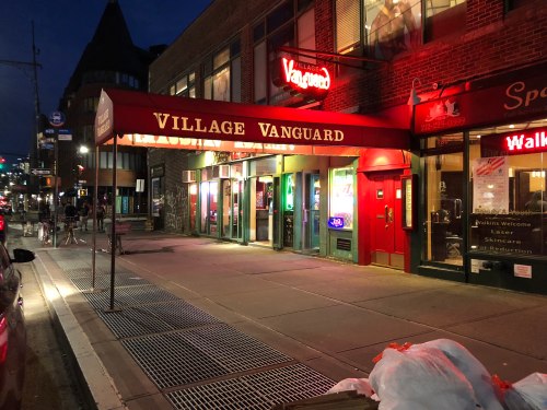 The Village Vanguard entrance at night, illuminated with red lights, showcasing a lively urban atmosphere.