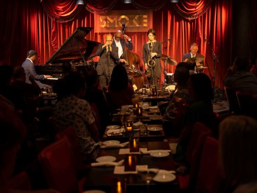 A jazz band performs on stage at Smoke Jazz Club, with an audience enjoying drinks and dinner at candlelit tables.