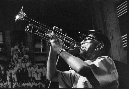 A musician plays the trumpet passionately on stage, captured in black and white.