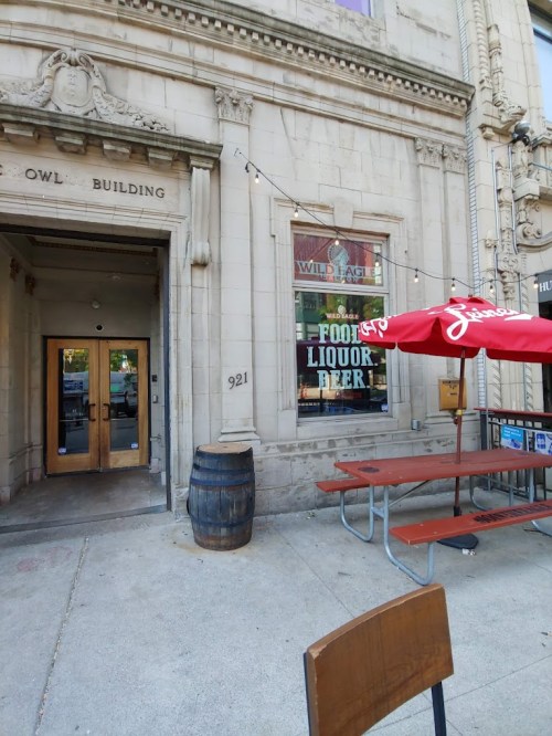 Entrance to the Owl Building with a sign for Wild Eagle, featuring outdoor seating and a barrel.