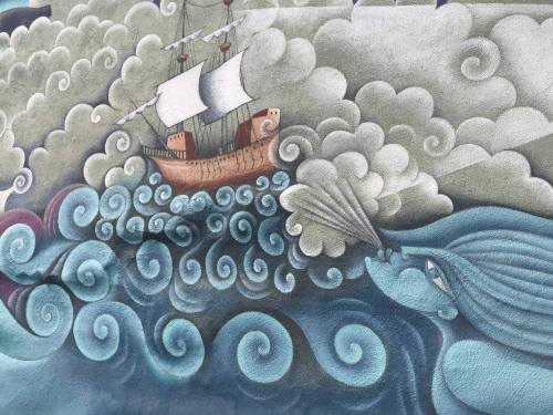 A colorful mural depicting a ship sailing through swirling waves, with a large fish blowing clouds.