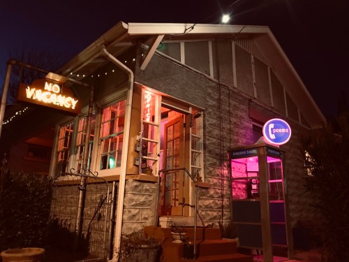 A cozy building at night with a "No Vacancy" sign, colorful lights, and a vintage phone booth outside.