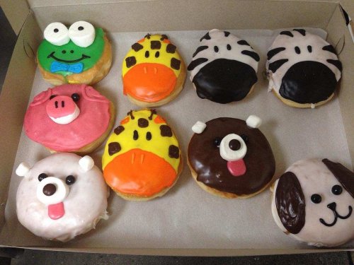 A box of colorful, animal-themed donuts featuring a frog, pig, giraffe, zebra, bear, and dog designs.