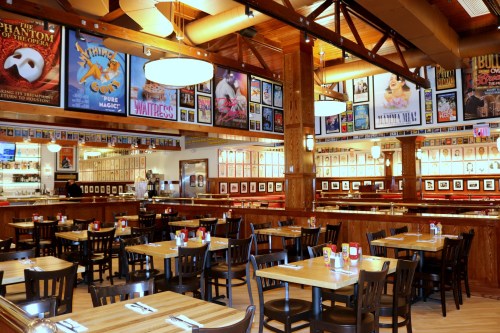 A cozy restaurant interior with wooden tables, chairs, and walls adorned with theater posters and framed photos.