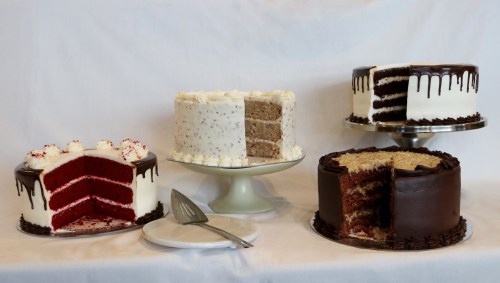 Four beautifully decorated cakes on display: red velvet, white cake with sprinkles, and two chocolate cakes, one sliced.