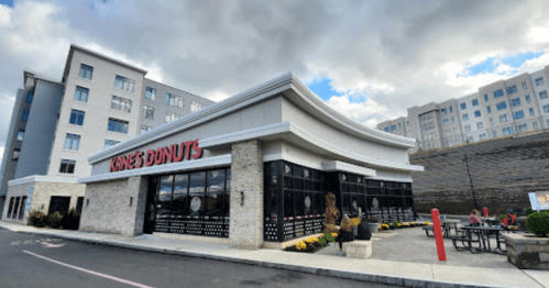 Exterior of Kane's Donuts with a modern building in the background and outdoor seating area.