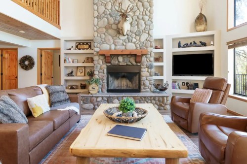 Cozy living room with a stone fireplace, leather furniture, wooden accents, and a large window letting in natural light.