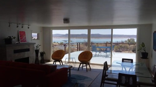 A modern living room with two yellow chairs, a red couch, and large windows showcasing a scenic lake view.
