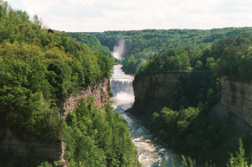 A scenic view of a waterfall cascading into a river, surrounded by lush green forests and steep cliffs.
