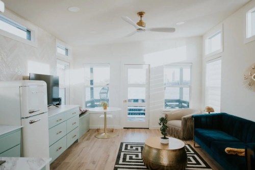 Bright, modern living space with a blue couch, gold accents, and large windows overlooking a balcony.