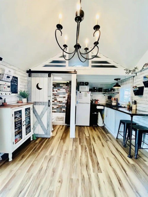 Cozy kitchen with wooden floors, a chandelier, and rustic decor, featuring a fridge and open shelving.