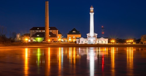 Historic Louisville Water Tower and pumping station at night with lights reflecting on the Ohio River.