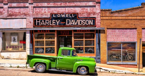 A vintage green pickup truck in front of a historic Harley-Davidson, featuring retro signage in Lowell Ghost Town, near Bisbee, Arizona.