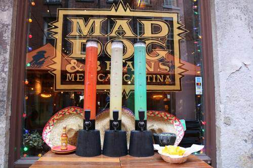 Three colorful drink dispensers in front of a restaurant window, with sombreros and chips nearby.
