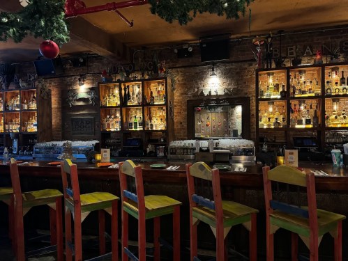 A cozy bar with wooden stools, shelves of liquor bottles, and festive decorations in a warm, inviting atmosphere.