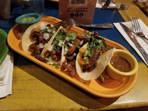 Three tacos filled with seasoned meat, topped with onions and cilantro, served with salsa and green sauce on a colorful plate.