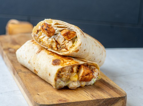 Two grilled chicken burritos, filled with cheese and vegetables, resting on a wooden cutting board.