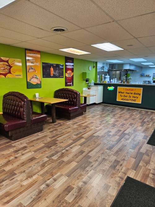 Interior of a casual eatery with green walls, wooden flooring, and cozy booths. Signs warn about addictive food.
