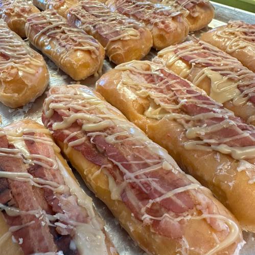 A tray of glazed donuts topped with strips of bacon and drizzled with a creamy icing.