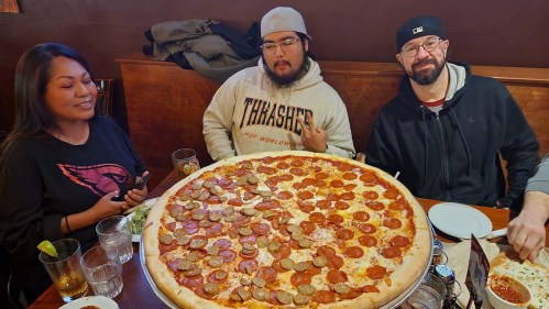 A group of three friends enjoying a large pizza with pepperoni and sausage at a restaurant.