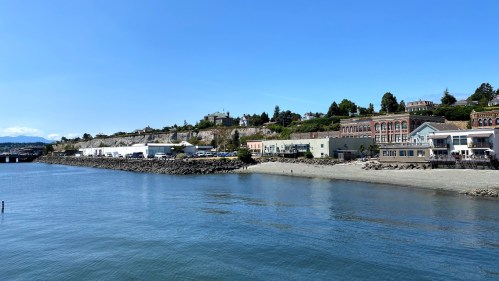 A calm waterfront scene with buildings along the shore under a clear blue sky.
