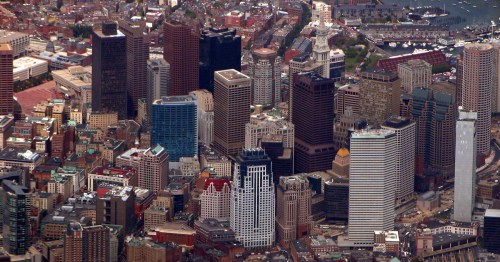 Aerial view of a bustling city skyline featuring tall buildings and a harbor in the background.