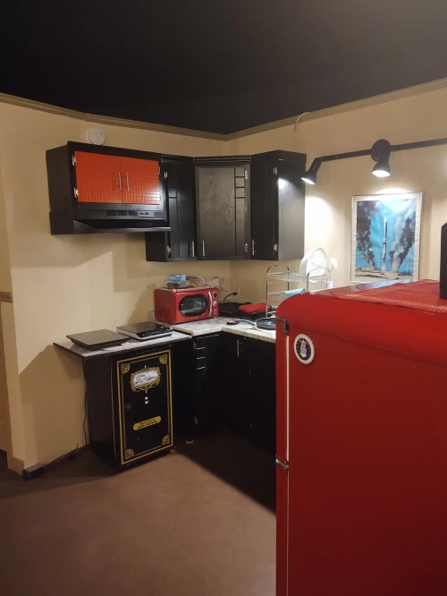 A modern kitchen featuring black cabinets, a red fridge, a microwave, and a colorful wall art piece.