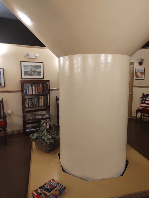 A large, white column in a cozy room with bookshelves, framed pictures, and a small table with magazines.