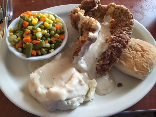A plate featuring fried chicken with gravy, mashed potatoes, a biscuit, and a side of mixed vegetables.