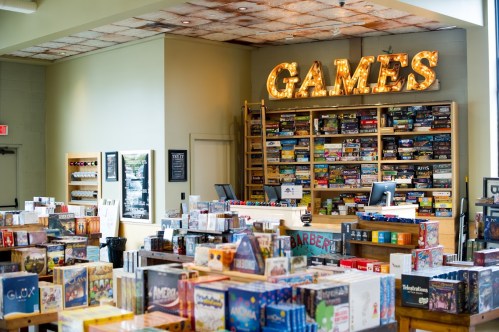 A vibrant game store filled with shelves of board games and a bright "GAMES" sign overhead.