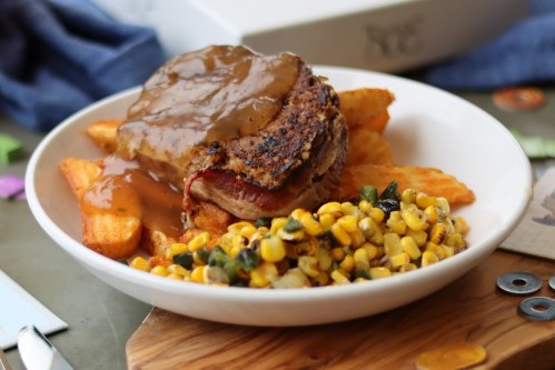 A plate of crispy fries topped with a savory meat dish and gravy, accompanied by a side of corn salad.