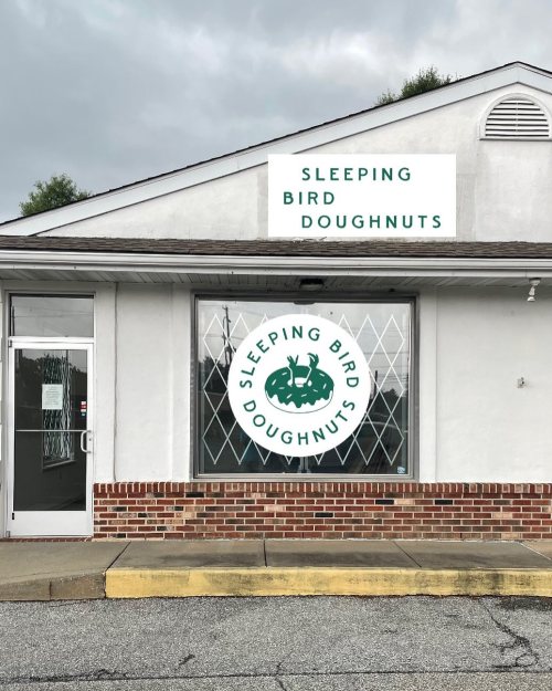 Exterior of a shop with a sign reading "Sleeping Bird Doughnuts" and a large circular logo on the window.