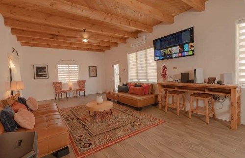 Cozy living room with wooden beams, a large TV, comfortable seating, and a decorative rug.