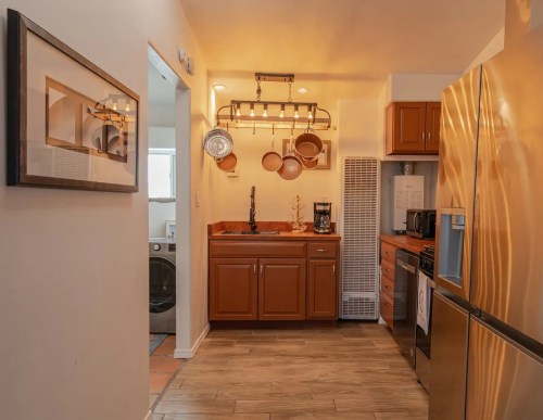 Cozy kitchen with wooden cabinets, stainless steel appliances, and a pot rack, featuring warm lighting and a laundry area.