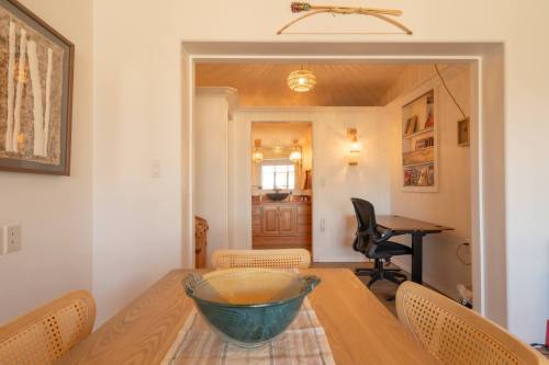 A cozy dining area with a wooden table, a decorative bowl, and a view into a well-lit kitchen and workspace.
